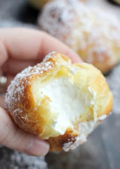 a hand holding a powdered sugar doughnut in front of other pastries on a baking sheet