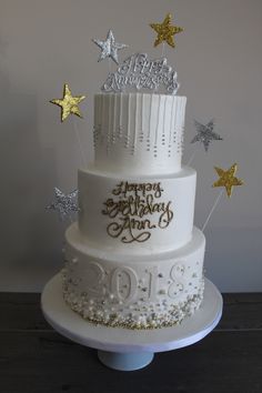 a three tiered white cake with gold stars on top and happy birthday written on the side