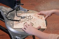 a person working on a piece of wood with a machine in front of it and some wire