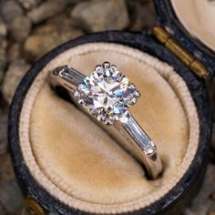 an engagement ring with two baguets on it in a velvet box next to some rocks