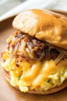 a close up of a sandwich on a wooden plate with cheese and onions in the middle