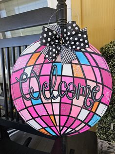 a pink and black welcome sign with polka dots on the top, hanging from a lamp post