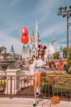 a woman sitting on top of a metal fence next to a red balloon in front of a castle