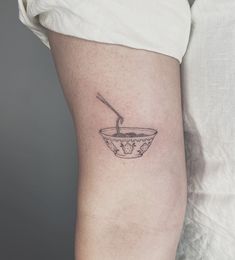 a woman's arm with a small bowl and spoon tattoo on the left thigh