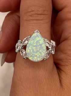 a woman's hand holding a ring with an opal and diamonds on it