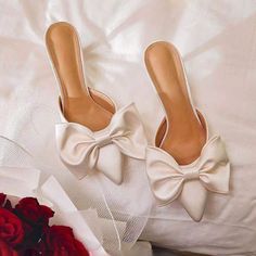 a pair of white high heeled shoes next to a bouquet of red roses on a bed