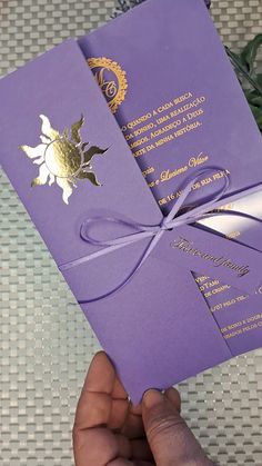 a person holding up a purple and gold wedding card with a bow on it's side