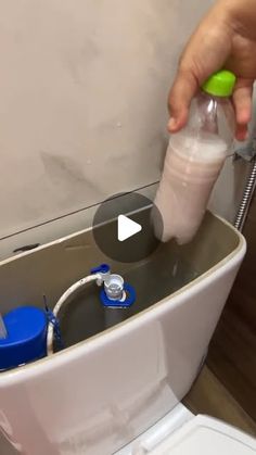 a person is using a bottle to fill up a toilet with water and soap in it