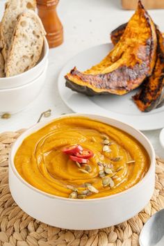 there is a bowl of soup on the table with other dishes and breads in the background