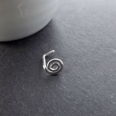 a small silver spiral earring sitting on top of a gray table next to a white cup