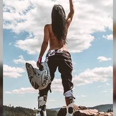 a person standing on top of a rock with a skateboard in their hand and wearing rollerblades