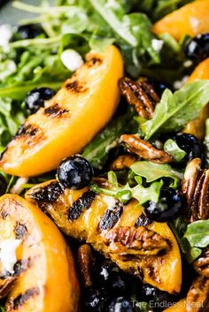 a salad with grilled peaches, blueberries and pecans on top is shown