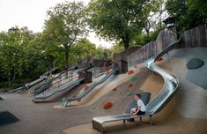 a man sitting on top of a slide next to a park filled with lots of trees