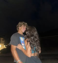 a young man and woman standing next to each other in front of a house at night