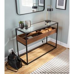 a glass table with drawers under a mirror and a purse on the floor next to it