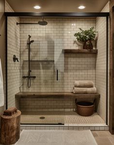 a walk in shower sitting next to a white rug and wooden stool on top of a tiled floor