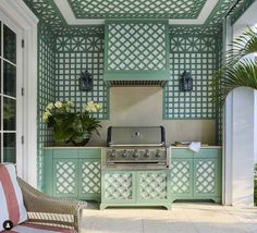 an outdoor kitchen with green painted cabinets and a grill in the center, surrounded by potted plants