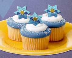 three cupcakes with frosting and stars on them sitting on a yellow plate