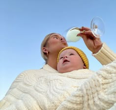 a woman holding a wine glass next to a man in a white sweater and yellow hat