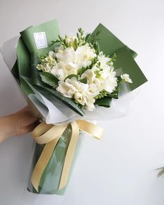 a bouquet of flowers is wrapped in green wrapping paper and being held by someone's hand