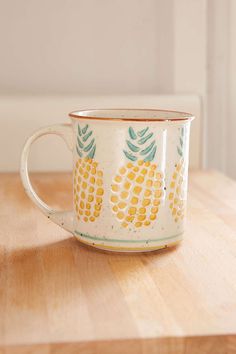 a white and yellow coffee cup sitting on top of a wooden table next to a wall