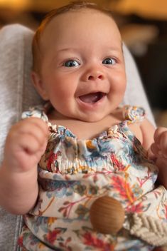 a baby is smiling while sitting in a highchair with her hands up to her chest