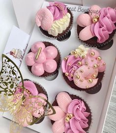 pink and white cupcakes in a box with gold decorations on top, decorated with flowers