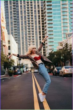 a woman is standing on one leg in the middle of an empty street with tall buildings behind her