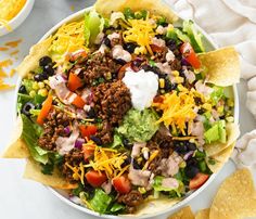 a bowl filled with taco salad next to tortilla chips and sour cream