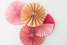 three pink and gold paper fans on a white background