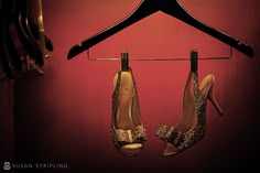 two pairs of high heeled shoes hanging on a hanger in front of a red wall