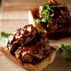 two pieces of bread with meat and sauce on them sitting on a cutting board next to parsley