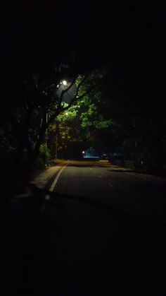 an empty street at night with the lights on and trees in the dark behind it