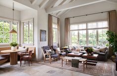 a living room filled with lots of furniture next to large windows and wooden tables in front of them