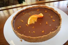 a chocolate tart with an orange slice on top sits on a white plate, ready to be eaten