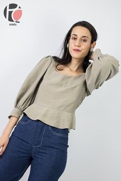 a woman is posing with her hands behind her head and wearing jeans, a gray top and earrings