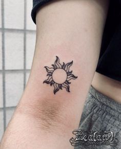 a small sun tattoo on the left inner arm, with a circle in the middle