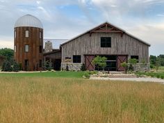 an old barn sits in the middle of a field with two silos behind it