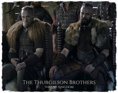 two men sitting next to each other in front of people wearing armor and furs