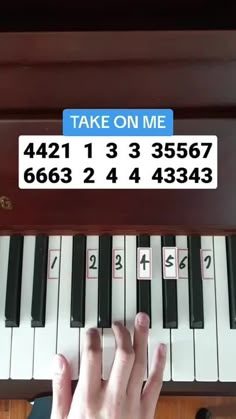 someone is playing the piano with their hand on it's keys, and there is a sign above them that says take on me