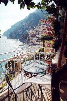 an outdoor table and chairs on a balcony next to the water with houses in the background