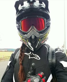 a person wearing a helmet and gloves on the side of the road with their hand in her pocket