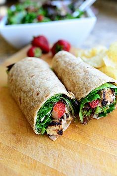 a wrap that is cut in half and sitting on a cutting board next to chips