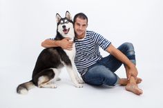 a man sitting on the ground with his dog in front of him and smiling at the camera