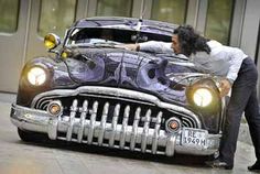 a man standing next to an old car with the hood painted like a batmobile