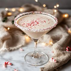 a white drink with candy canes in it on a marble table next to christmas lights