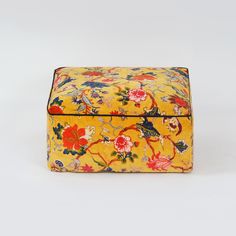 a yellow floral box sitting on top of a white table next to a red and blue object