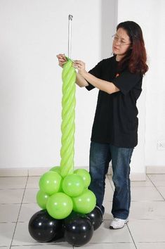 a woman standing in front of a green balloon column with black balloons on it and one person holding an object