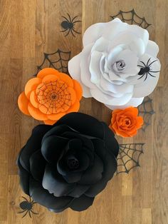 three paper flowers sitting on top of a wooden floor next to spider webs and pumpkins