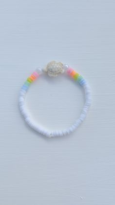 a white beaded bracelet with a shell and rainbow colored beads on the end of it